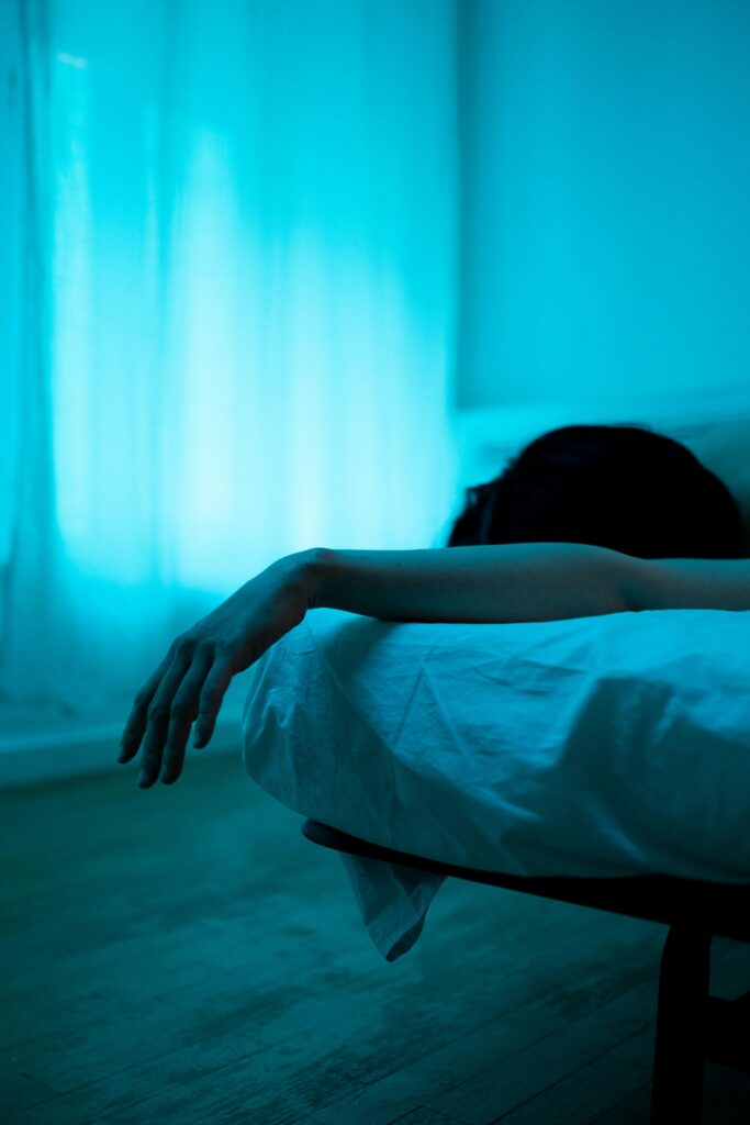 A person lying on a bed in soft blue lighting, one arm hanging gently off the side, creating a quiet, introspective nighttime mood.